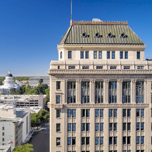 A grand classical building with a triangular pediment and columns rises against a clear blue sky, viewed from an elevated angle.