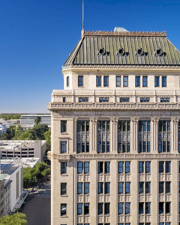 A grand classical building with a triangular pediment and columns rises against a clear blue sky, viewed from an elevated angle.