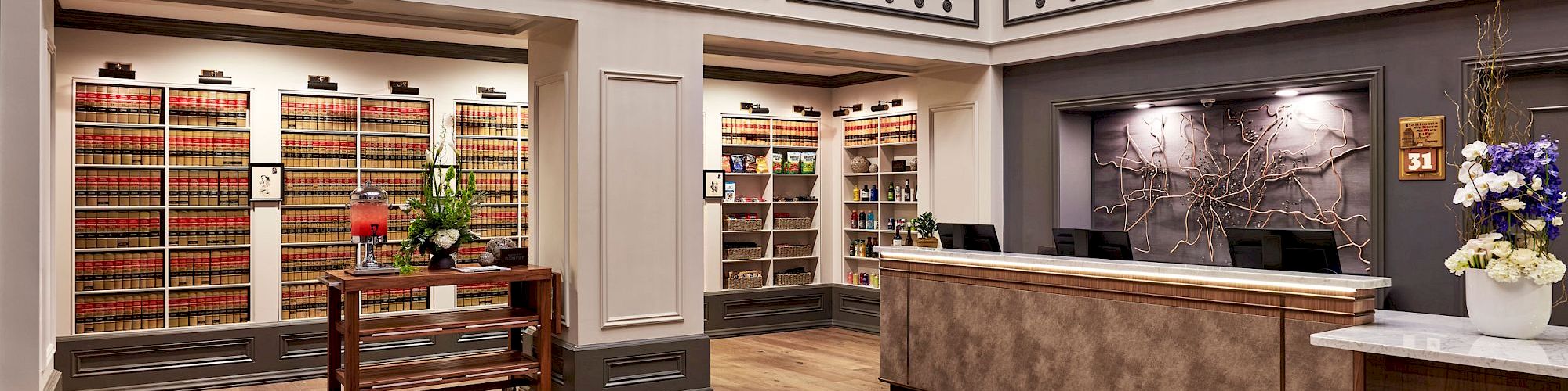 Luxury shop interior with tall shelves, wrought-iron balconies, a bright chandelier, and a reception desk facing decorative wall art.
